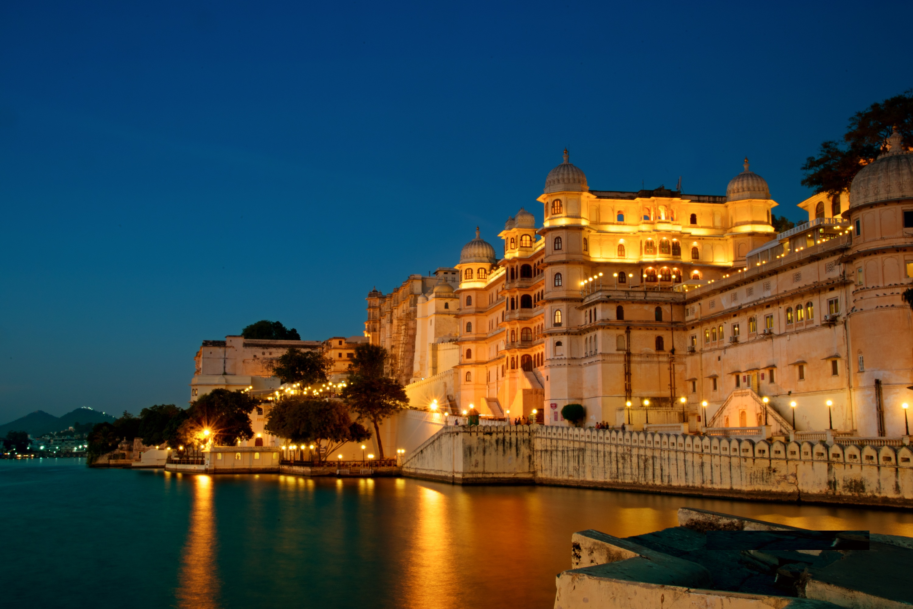 City Palace glowing beside Lake Pichola at dusk